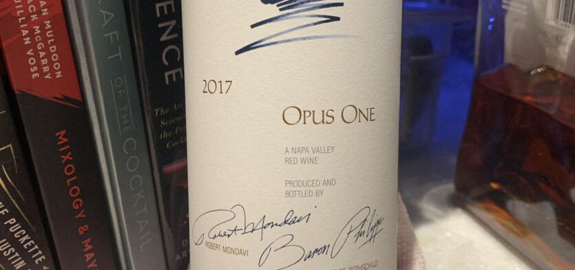 A bottle of Opus One wine in front of books.